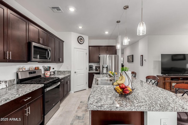 kitchen featuring visible vents, stainless steel appliances, dark brown cabinets, a sink, and an island with sink
