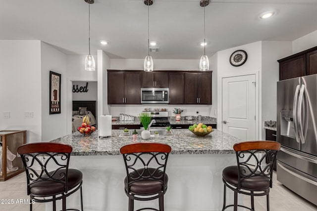 kitchen with dark brown cabinets, a breakfast bar area, appliances with stainless steel finishes, and stone counters