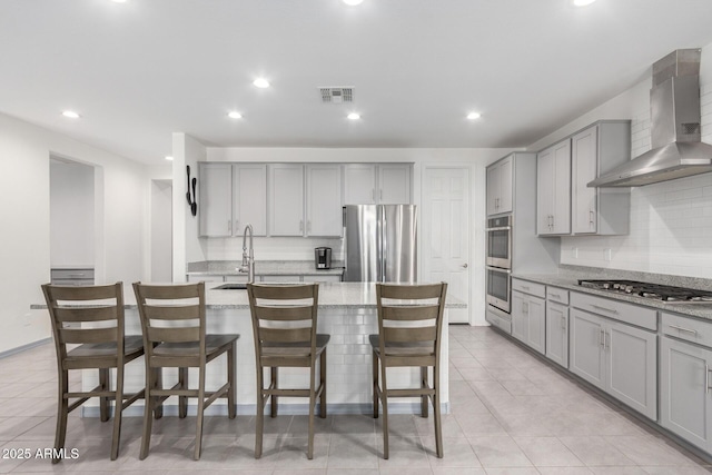 kitchen featuring visible vents, gray cabinets, a sink, stainless steel appliances, and wall chimney range hood