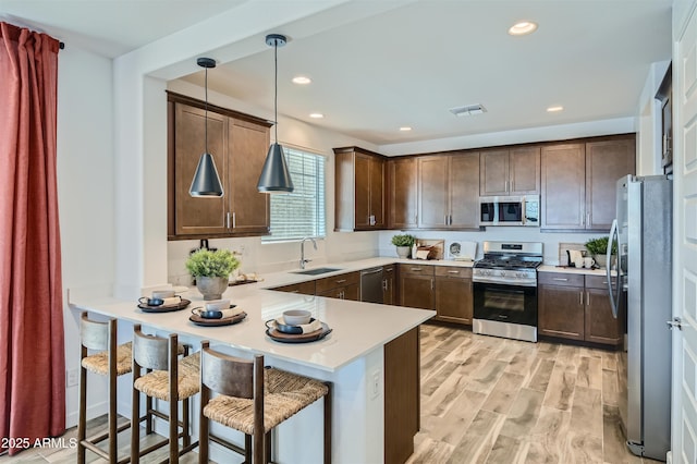 kitchen with kitchen peninsula, hanging light fixtures, sink, appliances with stainless steel finishes, and a breakfast bar area