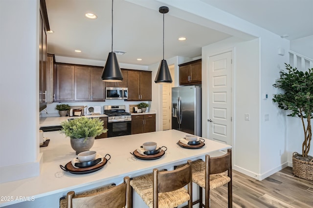 kitchen with appliances with stainless steel finishes, decorative light fixtures, light hardwood / wood-style floors, and dark brown cabinetry