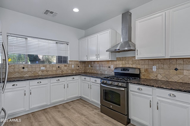 kitchen with stainless steel range with gas cooktop, wall chimney exhaust hood, white cabinetry, light wood finished floors, and backsplash