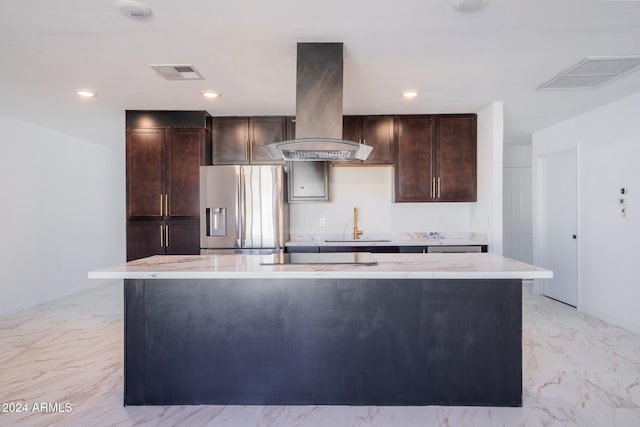 kitchen featuring dark brown cabinetry, stainless steel fridge, a center island with sink, and island range hood