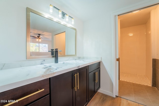 bathroom featuring a tile shower, vanity, hardwood / wood-style flooring, and ceiling fan