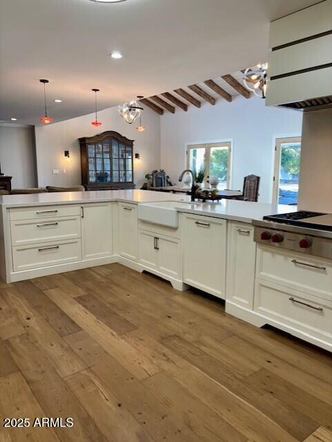 kitchen with decorative light fixtures, white cabinetry, wood-type flooring, stainless steel gas cooktop, and beam ceiling