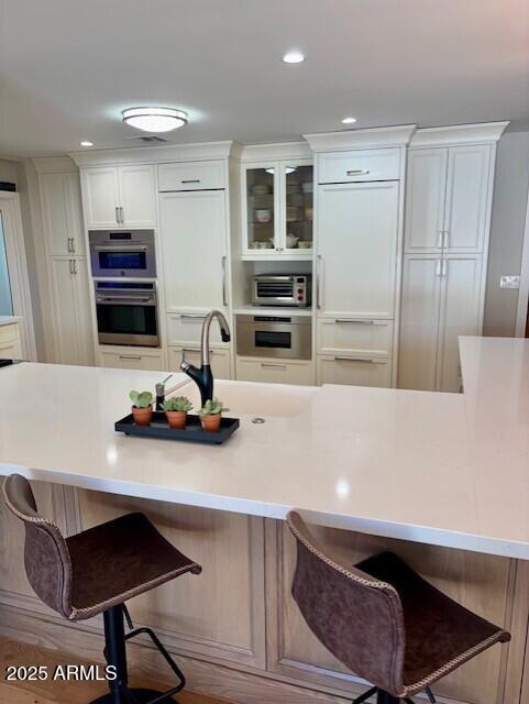 kitchen featuring stainless steel double oven, paneled built in fridge, a breakfast bar, and white cabinets