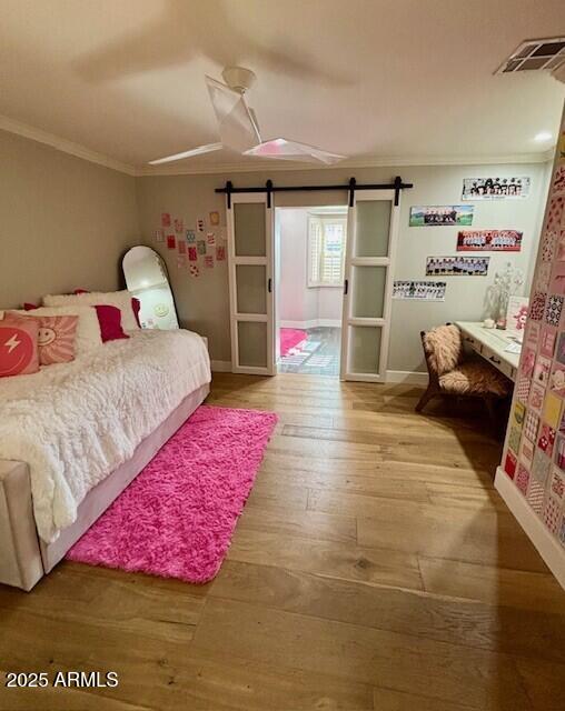 bedroom with ornamental molding, a barn door, hardwood / wood-style floors, and ceiling fan