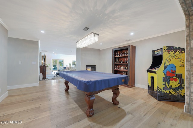 recreation room with a multi sided fireplace, ornamental molding, and light wood-type flooring