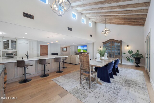 dining room featuring sink, beam ceiling, a towering ceiling, wooden ceiling, and light wood-type flooring