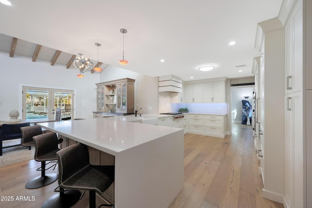 kitchen with light hardwood / wood-style flooring, white cabinetry, hanging light fixtures, a spacious island, and beamed ceiling