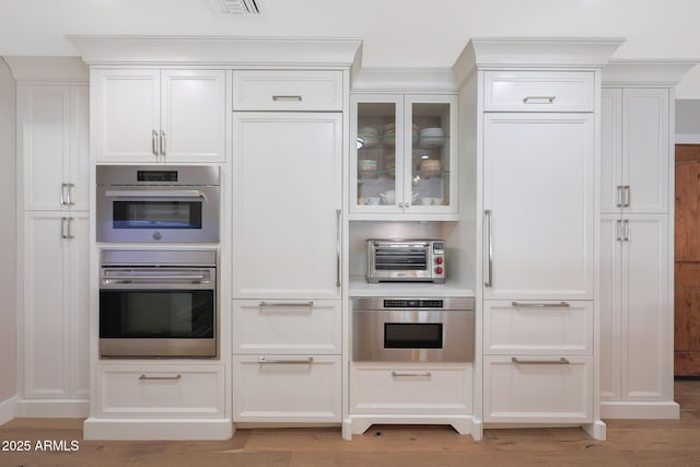 kitchen with white cabinetry, double oven, and light hardwood / wood-style flooring