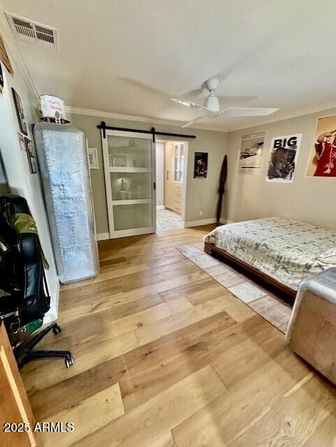 bedroom with crown molding, ceiling fan, a barn door, and hardwood / wood-style floors