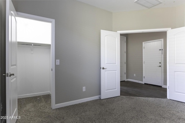 unfurnished bedroom with a spacious closet, a closet, and dark colored carpet