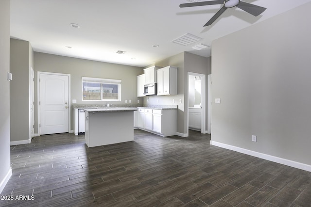 kitchen with light stone counters, ceiling fan, a kitchen island, and white cabinets