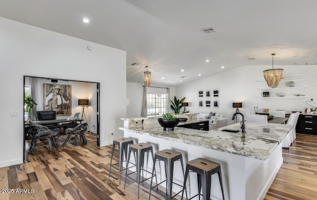 kitchen with lofted ceiling, a large island, a breakfast bar, wood finished floors, and a sink