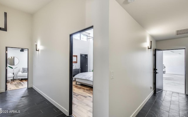 corridor with a towering ceiling, dark wood finished floors, visible vents, and baseboards