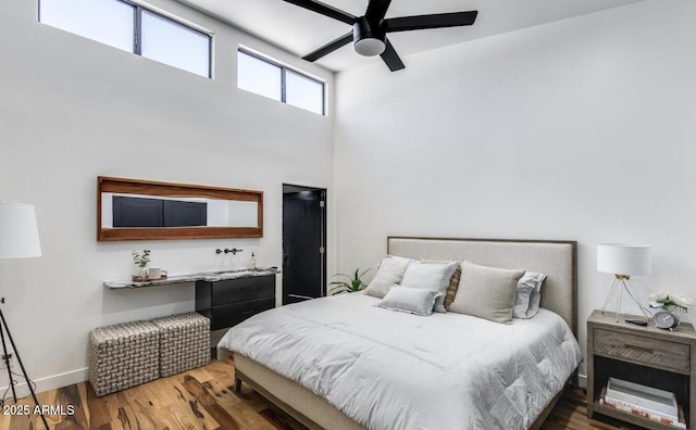 bedroom featuring ceiling fan, a high ceiling, baseboards, and wood finished floors