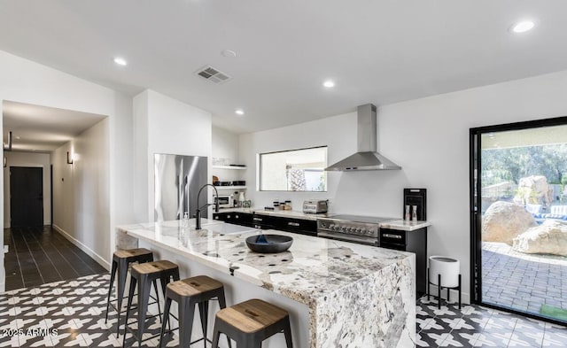 kitchen with visible vents, appliances with stainless steel finishes, a sink, wall chimney range hood, and a kitchen breakfast bar