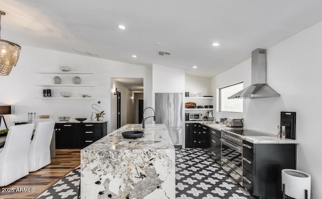 kitchen with visible vents, wall chimney exhaust hood, stainless steel refrigerator, dark cabinetry, and open shelves