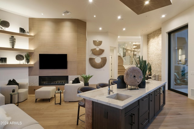 kitchen featuring sink, a kitchen breakfast bar, an island with sink, light hardwood / wood-style floors, and a fireplace