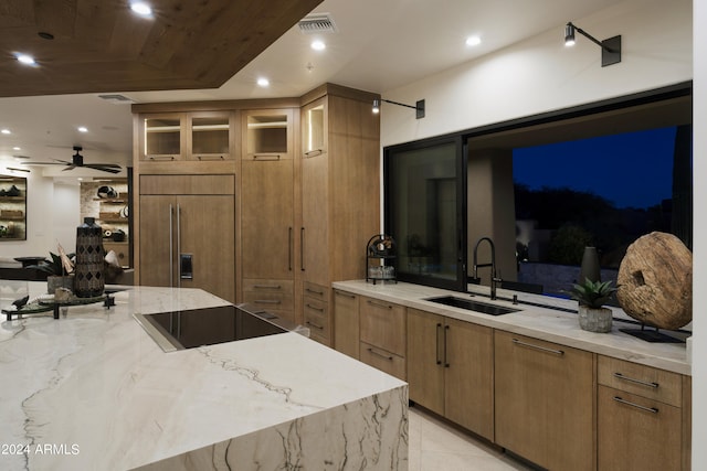 kitchen featuring light stone counters, black electric cooktop, ceiling fan, sink, and paneled built in fridge