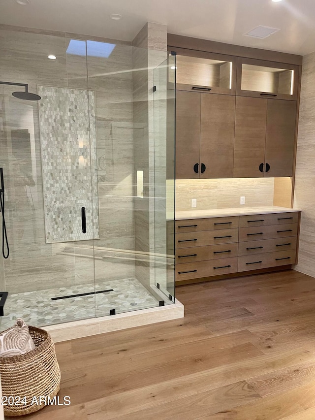 bathroom featuring vanity, a shower with door, a skylight, tasteful backsplash, and wood-type flooring