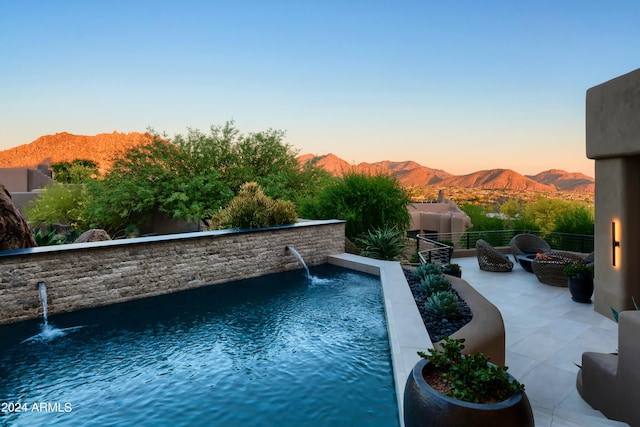 pool at dusk with a patio area, pool water feature, and a mountain view