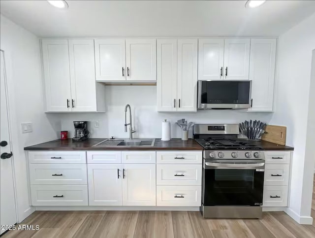 kitchen with dark countertops, appliances with stainless steel finishes, white cabinets, and a sink