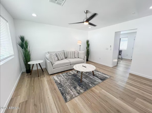 living area featuring a ceiling fan, visible vents, baseboards, and wood finished floors