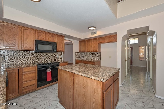 6928 W Oraibi Dr, Glendale, AZ 85308 - kitchen with black appliances, arched walkways, light stone counters, a center island, and brown cabinets