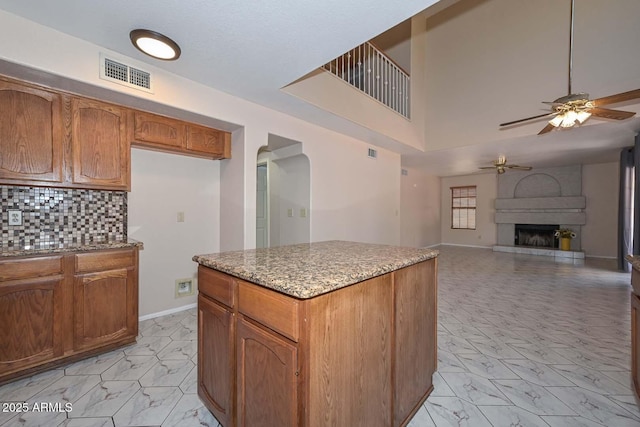6928 W Oraibi Dr, Glendale, AZ 85308 - kitchen with a ceiling fan, light marble finish floors, brown cabinetry, arched walkways, and a kitchen island