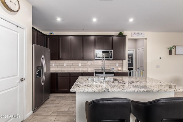 kitchen featuring tasteful backsplash, dark brown cabinetry, stainless steel appliances, and a sink