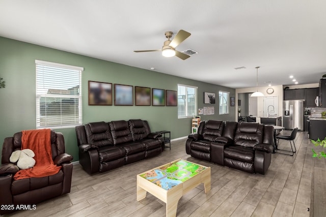 living room featuring baseboards, visible vents, light wood-type flooring, and ceiling fan