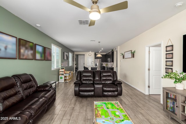 living area featuring baseboards, wood finished floors, visible vents, and ceiling fan