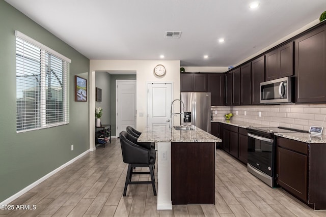 kitchen with tasteful backsplash, dark brown cabinetry, stainless steel appliances, and light stone counters