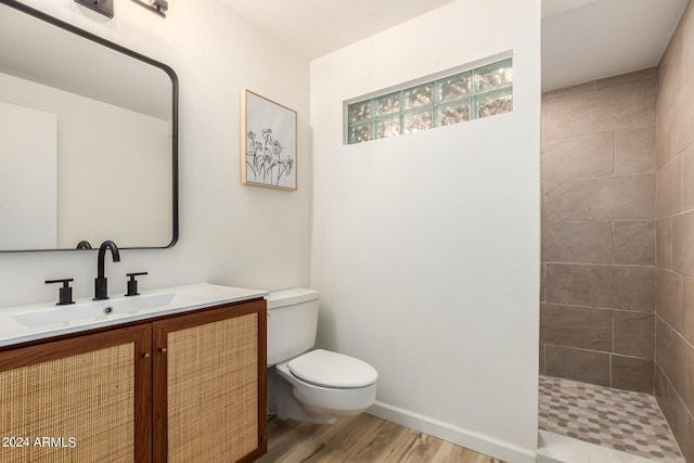 bathroom with a tile shower, hardwood / wood-style floors, vanity, and toilet