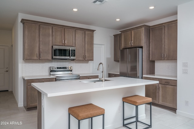 kitchen featuring backsplash, stainless steel appliances, sink, a breakfast bar area, and an island with sink