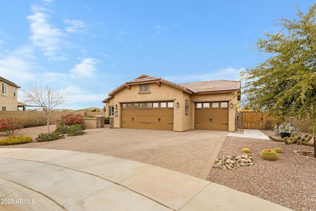 view of front of property featuring a tile roof, an attached garage, fence, decorative driveway, and stucco siding