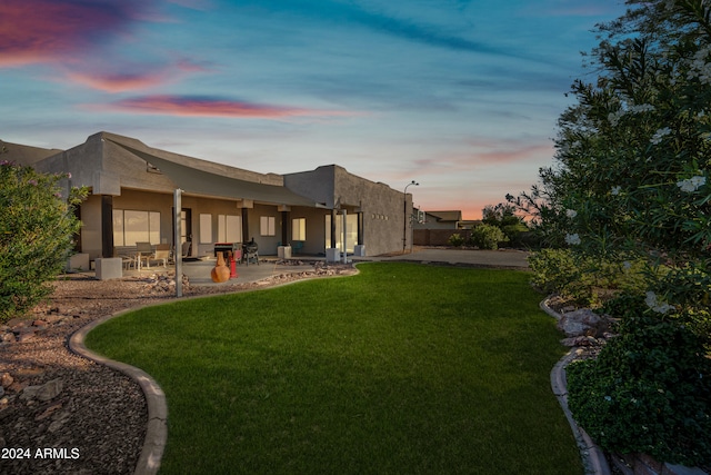 back house at dusk with a patio and a lawn