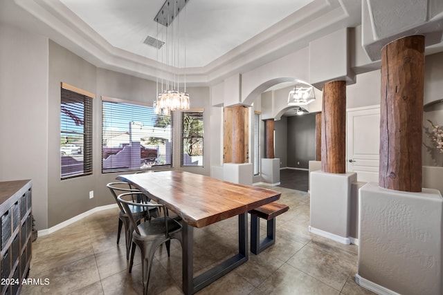 dining area featuring tile patterned floors, a raised ceiling, an inviting chandelier, and decorative columns