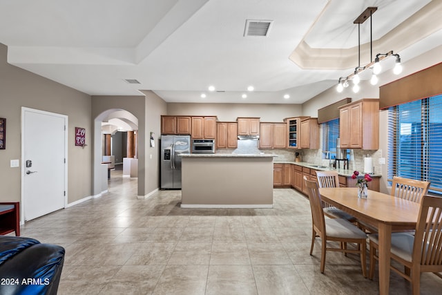 kitchen with stainless steel appliances, a center island, decorative backsplash, a tray ceiling, and pendant lighting