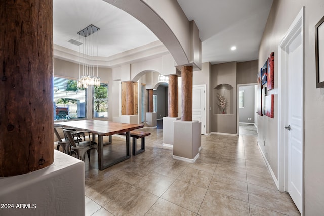 tiled dining area featuring ornate columns, a chandelier, and a tray ceiling