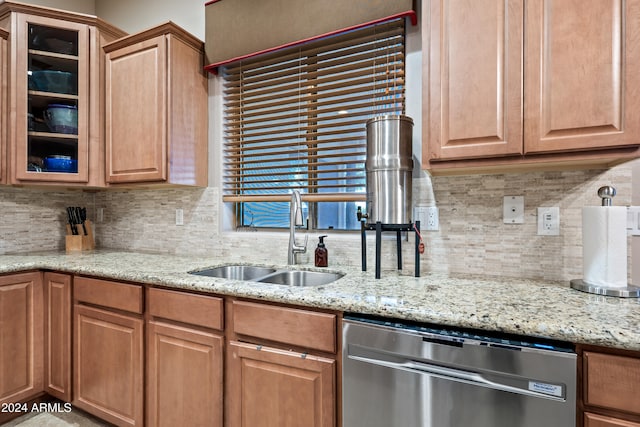 kitchen featuring tasteful backsplash, stainless steel dishwasher, sink, and light stone counters