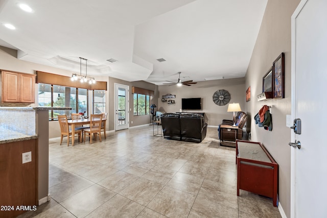 tiled living room with a tray ceiling and ceiling fan with notable chandelier