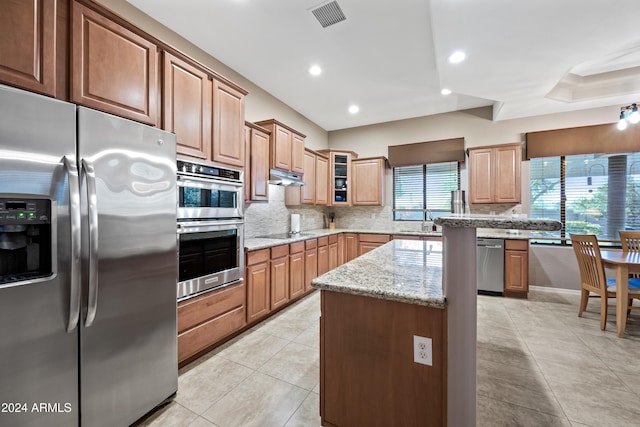 kitchen featuring appliances with stainless steel finishes, light stone countertops, light tile patterned floors, backsplash, and a center island