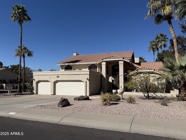 mediterranean / spanish-style house with an attached garage, a tile roof, concrete driveway, stucco siding, and a chimney