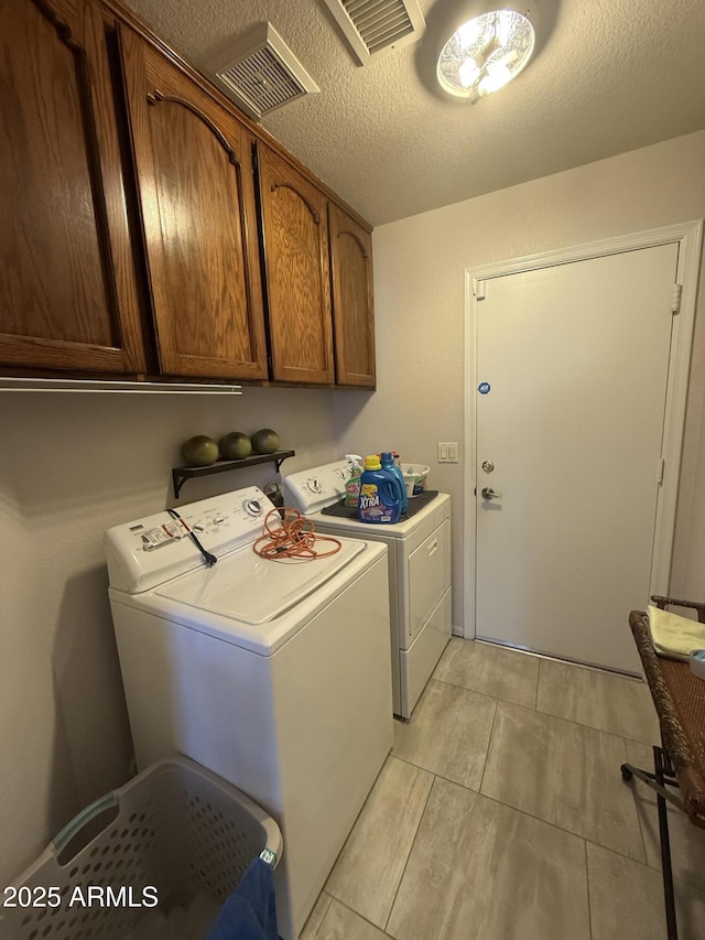 clothes washing area featuring cabinet space, visible vents, washer and clothes dryer, and a textured ceiling