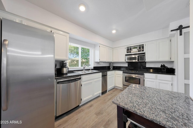 kitchen with sink, stainless steel appliances, light hardwood / wood-style floors, white cabinets, and a barn door