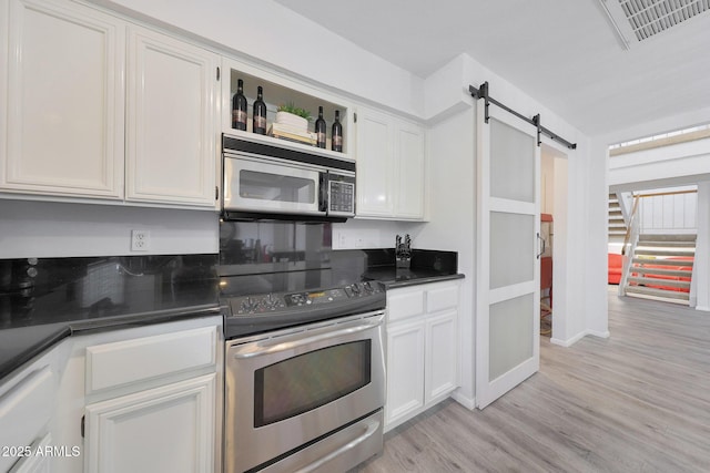 kitchen with a barn door, appliances with stainless steel finishes, white cabinets, and light hardwood / wood-style floors