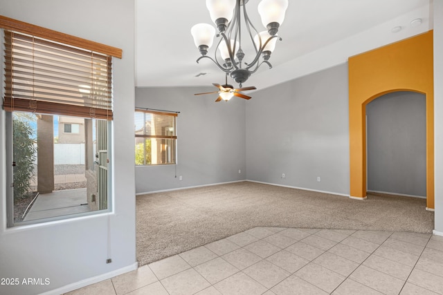 empty room featuring arched walkways, carpet flooring, ceiling fan with notable chandelier, and tile patterned floors